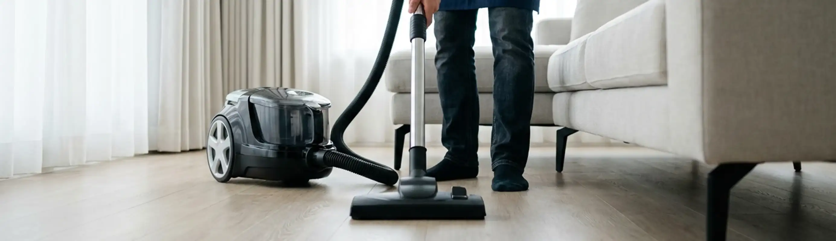 Professional house cleaner vacuuming a living room floor with a canister vacuum cleaner, St Paul, MN.