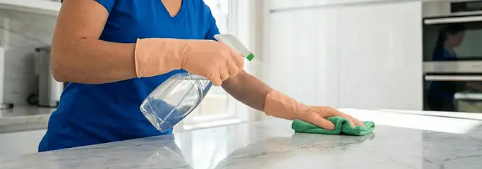 Maid service worker spraying and wiping a kitchen countertop with a microfiber cloth for sanitizing, St Paul, MN.