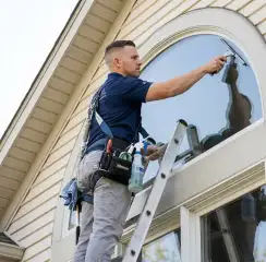 Professional window cleaner on a ladder using a squeegee to clean an exterior arched window, St Paul, MN.