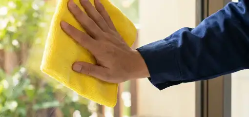 House cleaner wiping a glass window with a yellow microfiber cloth for streak-free cleaning, St Paul, MN.